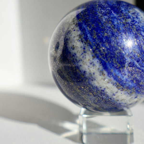 Solid gemstone ball in rich blue with natural white calcite veins and metallic gold pyrite sparkles, viewed from the side.